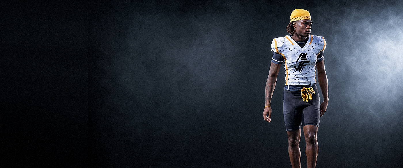 A football player photographed from behind under stadium lights at night, the JF grenade printed across the back of his jersey.